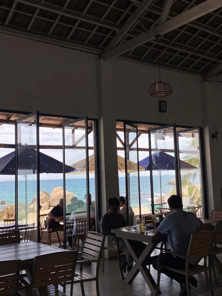 Guests dining beside floor-to-ceiling windows with a turquoise sea view